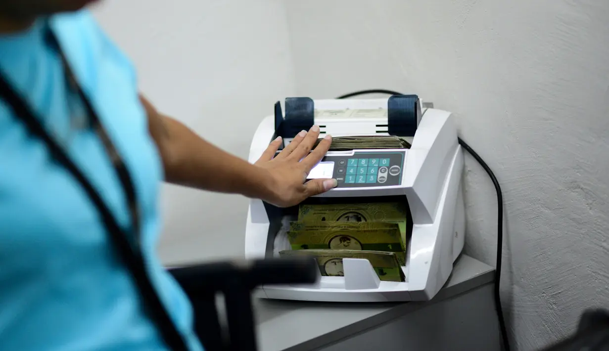 Seorang kasir menghitung mata uang lokal yang baru di Caracas, Venezuela (15/12). Inflasi parah melanda Venezuela membuat mata uang negara setempat tak bernilai, hingga akhirnya masyarakat lokal menciptakan mata uang sendiri. (AFP Photo/Federico Parra)