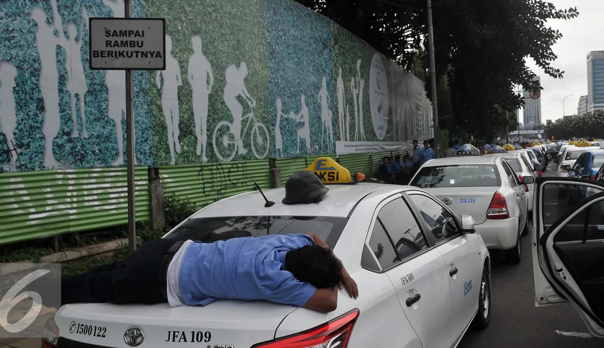 Seorang sopir tidur diatas bagasi taksi saat demo di depan Gedung DPR/MPR, Jakarta, Selasa (22/3). Selain melakukan demo, sopir taksi tersebut melakukan sweeping ke supir taksi yang beroperasi di dalam tol, dan membakar ban. (Liputan6.com/Johan Tallo)