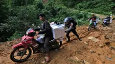 Seorang petugas polisi membantu petugas pemilu mendorong sepeda motor mendaki bukit saat mendistribusikan kotak suara dan perlengkapan pemilu lainnya ke tempat pemungutan suara (TPS) di desa-desa terpencil di Maros, Sulawesi Selatan, Selasa, 13 Februari 2024. (AP Photo/Masyudi S. Firmansyah)