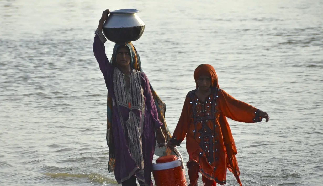 Wanita yang terkena banjir membawa air minum dalam wadah setelah melarikan diri dari banjir yang melanda rumah mereka setelah hujan lebat di daerah Sohbatpur di distrik Jaffarabad di provinsi Balochistan (29/8/2022). (AFP/Fida Hussain)