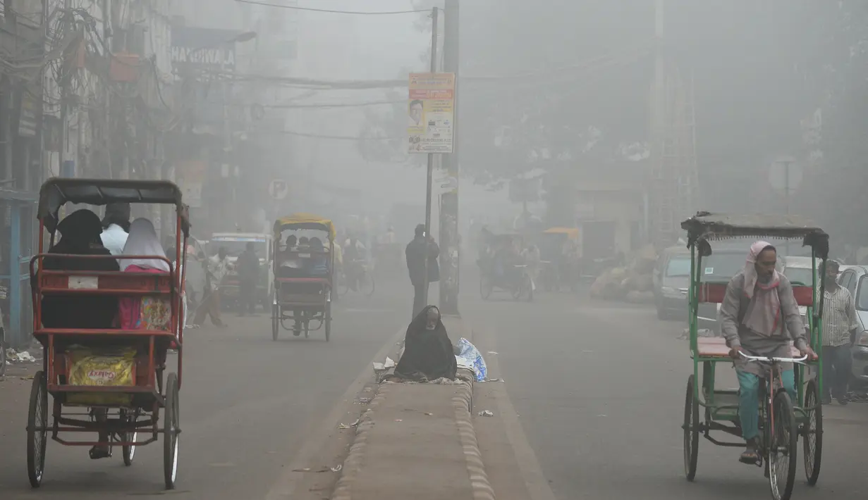 Seorang tunawisma India duduk di jalanan kota New Delhi yang diselimuti kabut asap, Rabu (8/11). Kabut asap tebal akibat polusi udara yang parah menyebabkan aktivitas di pusat kota New Delhi lumpuh seketika. (SAJJAD HUSSAIN/AFP)