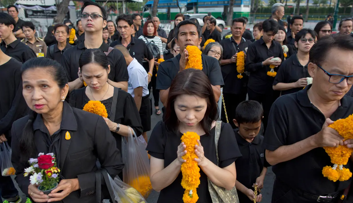 Warga Thailand mengenakan pakain hitam dan membawa bunga saat memberi penghormatan untuk mendiang Raja Thailand Bhumibol Adulyadej di luar Grand Palace, Bangkok, Thailand (13/10). (AP Photo/Gemunu Amarasinghe)