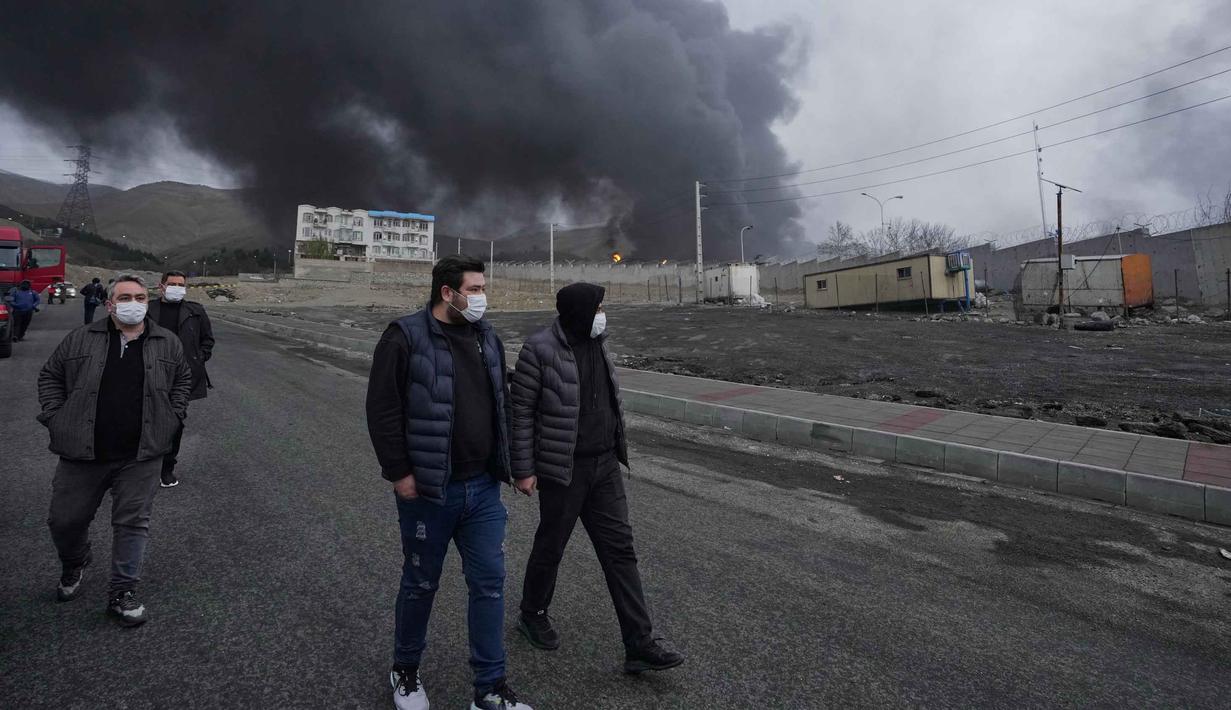 Media lokal Iran melaporkan kebakaran besar terjadi di Teheran dan mengonfirmasi bahwa kilang minyak dan fasilitas penyimpanan minyak terkena dua rudal serangan udara. Tampak dalam foto, empat pria berjalan berlatar kepulan asap tebal dari serangan gabungan AS-Israel terhadap fasilitas penyimpanan minyak pada Sabtu 7 Maret 2026 malam yang membubung ke langit di Teheran, Minggu, 8 Maret 2026. (AP Photo/Vahid Salemi)