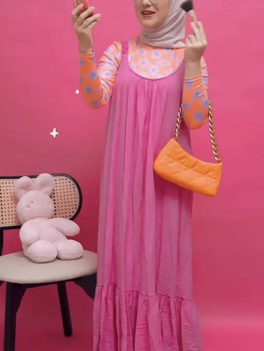 Irish tampil mengenakan dress pink dipadukan inner long sleeve motif warna orange yang serasi dengan tasnya. Iris memadukannya dengan hijab warna serasi, lengkap dengan kacamatanya. (@_irishbella_)