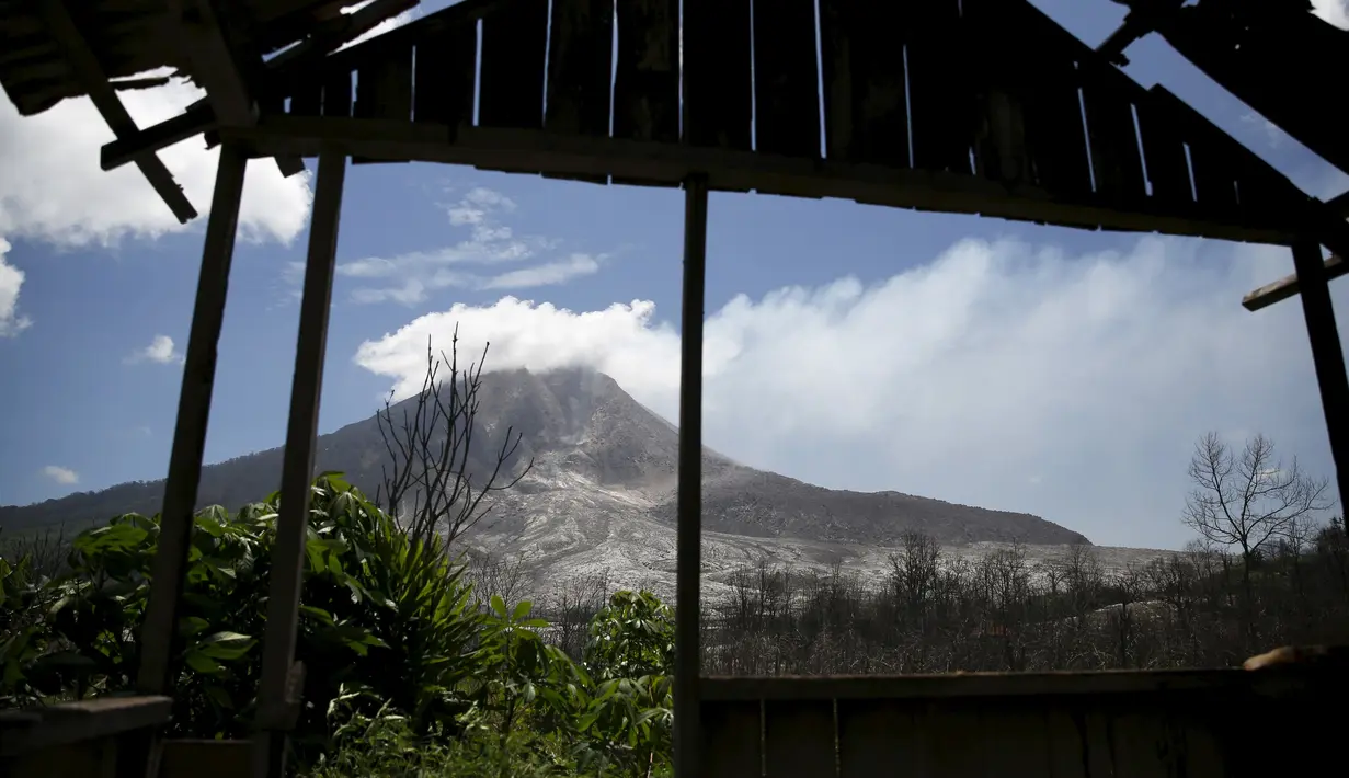 Gunung Sinabung terlihat dari puing rumah yang rusak akibat erupsi di Beras Tepu Desa, Karo, Sumatera Utara, 21 Juni 2015. Ribuan warga yang tinggal di sekitar lereng Gunung Sinabung meninggalkan rumah mereka. (REUTERS/Beawiharta)