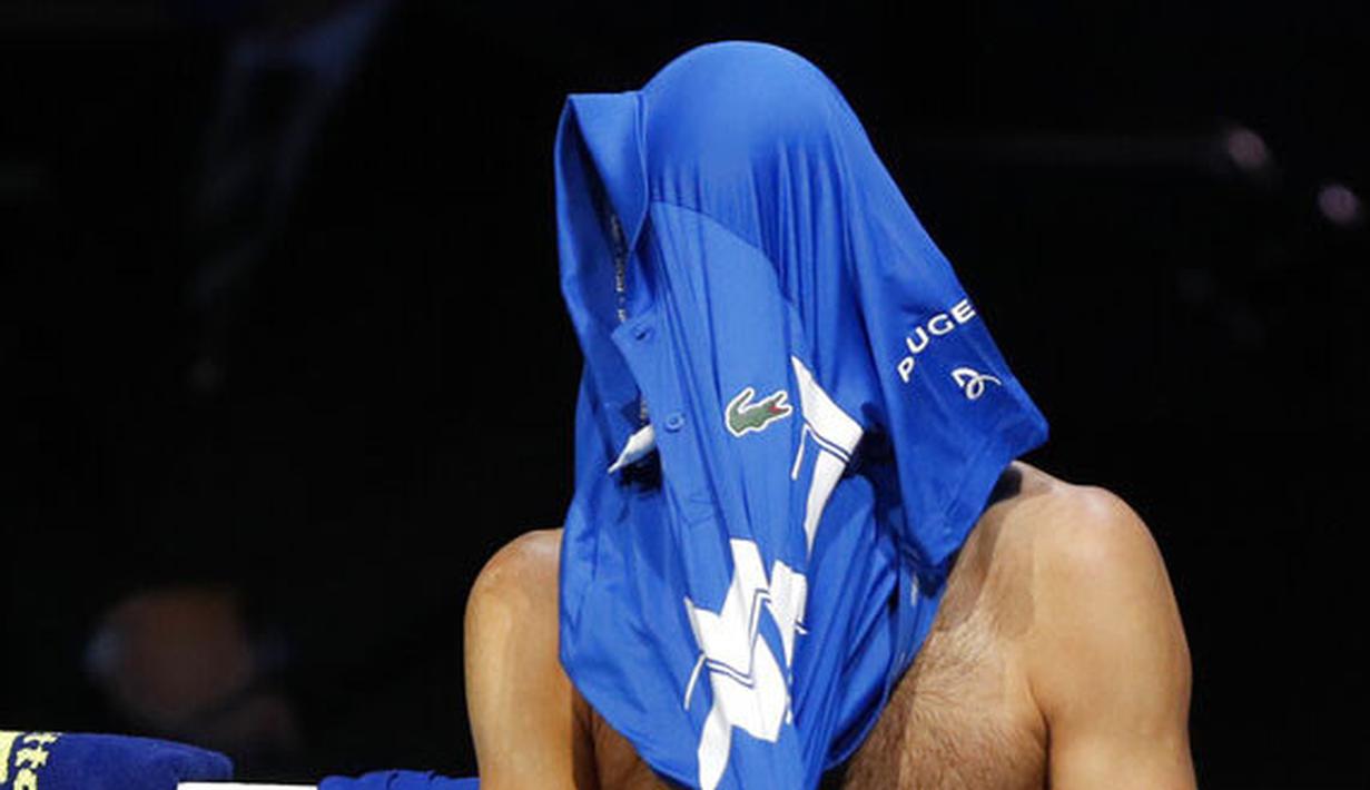 Petenis Serbia, Novak Djokovic, menutup wajahnya dengan baju usai ditaklukkan Petenis Rusia, Daniil Medvedev, pada ATP Finals di O2 Arena, London, Kamis (19/11/2020). Petenis nomor satu dunia itu takluk 3-6 3-6. (AP/Frank Augstein)