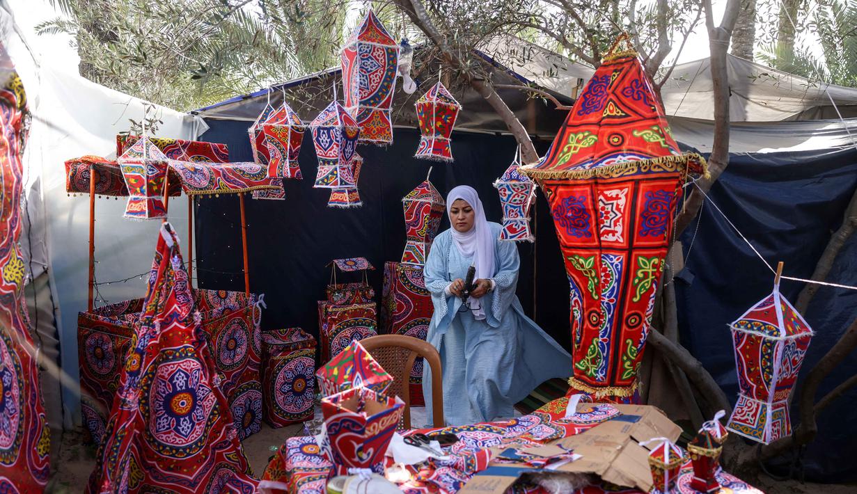 Fanous menjadi simbol suka cita, harapan, dan tradisi yang tetap bertahan di tengah situasi konflik berkepanjangan antara Israel dan Hamas. Tampak dalam foto, Rehan Hazem Sharab, seorang pengungsi Palestina berusia 32 tahun, membuat lampion dan barang-barang lainnya dari kotak bantuan yang tersisa sebagai persiapan menyambut bulan suci Ramadan yang dimulai pada 17 Februari, di luar tendanya di lingkungan Al-Mawasi, Khan Younis, di Jalur Gaza selatan pada Sabtu 7 Februari 2026. (Bashar Taleb/AFP)