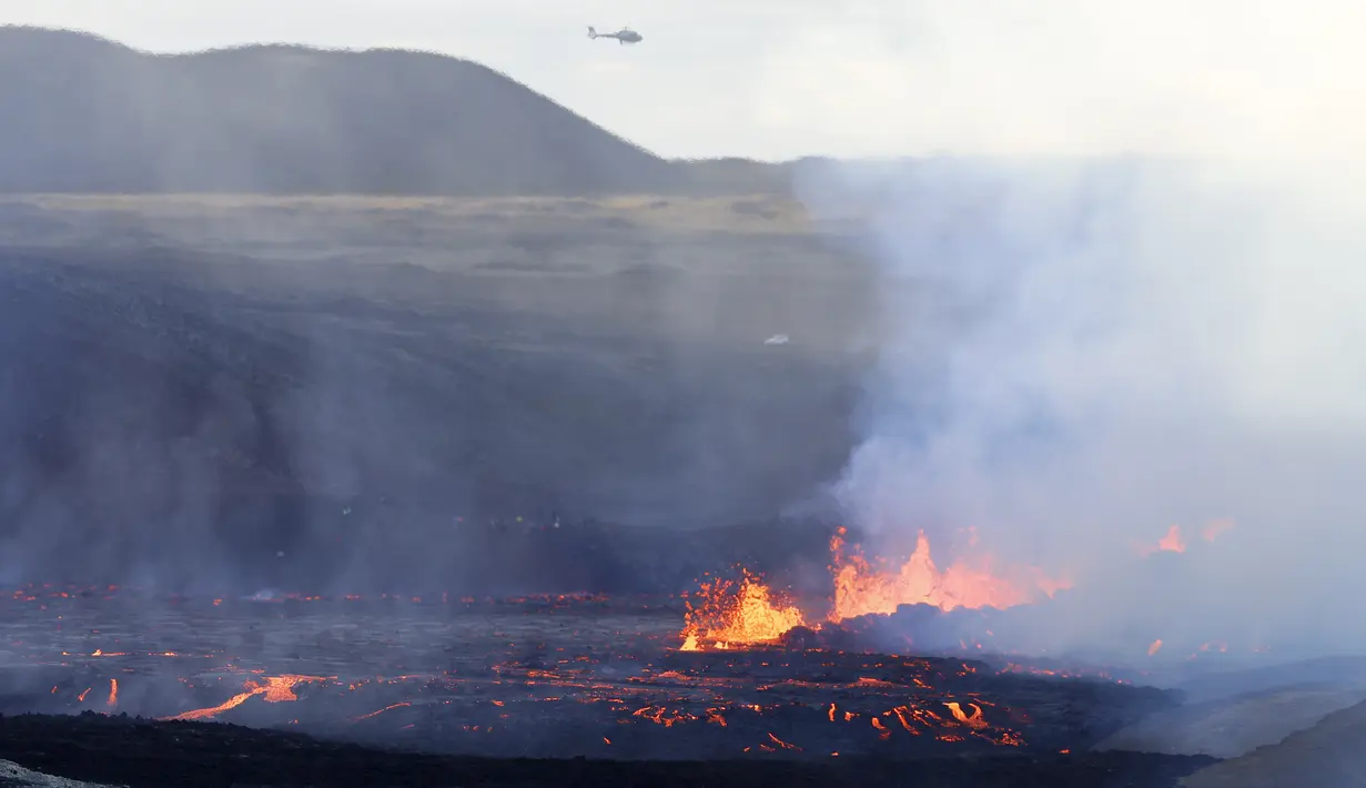 Sebuah helikopter terbang di dekat gunung berapi Fagradalsfjall di Islandia pada Rabu 3 Agustus 2022, yang terletak 32 kilometer (20 mil) barat daya ibukota Reykjavik dan dekat dengan Bandara Internasional Keflavik. Erupsi tersebut menjadi daya tarik wisatawan dan penonton yang berbondong-bondong ke tempat kejadian. (AP Photo/Brynjar Gunnarsson)