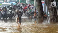 Anak-anak bermain air saat banjir meggenangi Jalan Raya Bogor di depan Pasar Induk Kramat Jati, Jakarta, Kamis (30/11/2023). (merdeka.com/Arie Basuki)