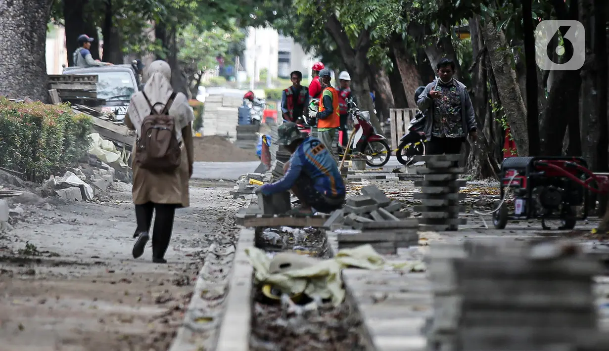 Pejalan kaki melintas saat pekerja menyelesaikan proyek revitalisasi pedestrian di kawasan Jalan Pattimura, Jakarta, Rabu (8/6/2022). Dinas Bina Marga DKI Jakarta merevitalisasi pedestrian dengan memperlebar menjadi tiga meter sehingga cukup luas untuk memberikan kenyamanan para pejalan kaki. (Liputan6.com/Faizal Fanani)