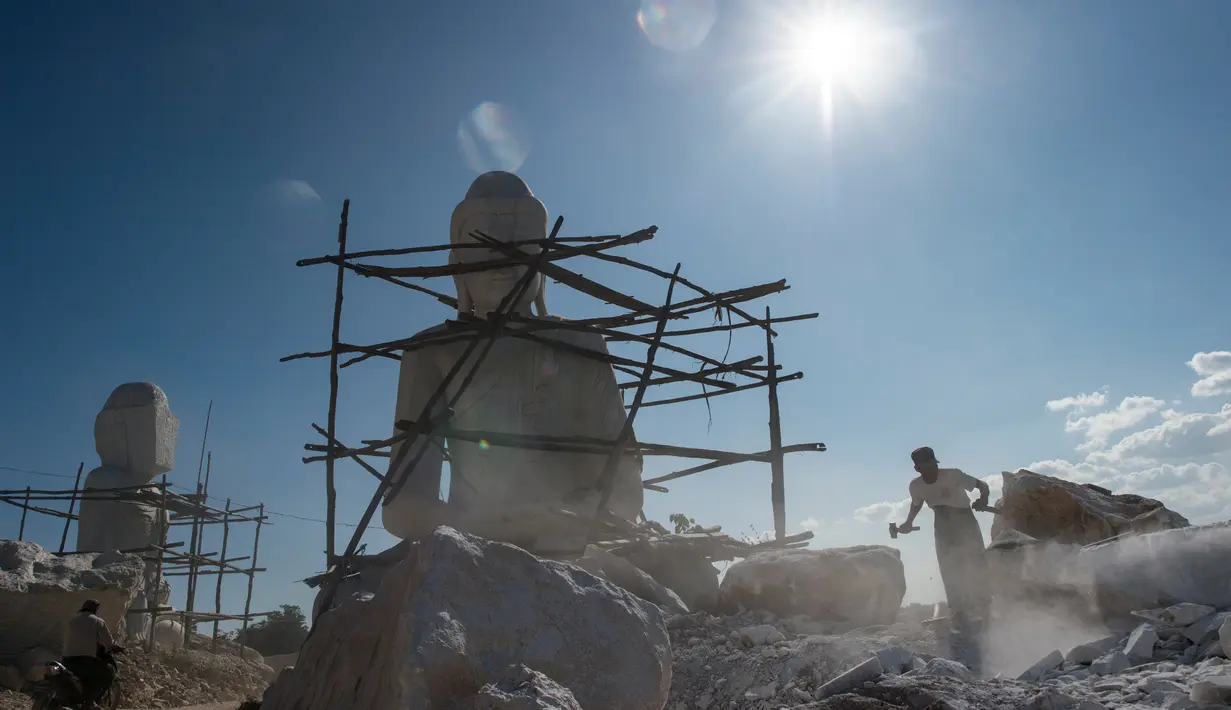 Seorang pria memecahkan batu di dekat patung Buddha di desa Sagyin, Madaya, Myanmar pada 22 Desember 2018.  Patung-patung marmer yang diproduksi di desa Sagyin ini diekspor ke Thailand, Vietnam, dan Taiwan. (YE AUNG THU / AFP)
