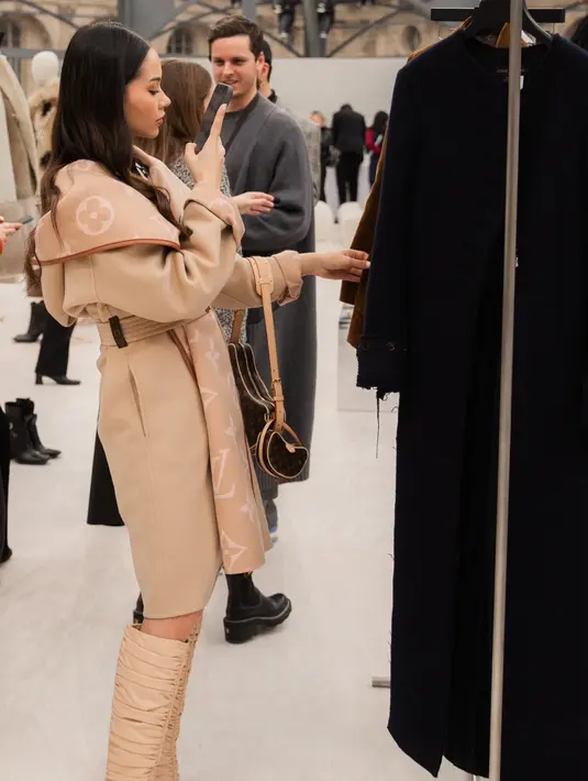 Ia mengenakan minidress putih dan outline hitam dengan high boots dan wool coat cokelat. [@alyssadaguise]