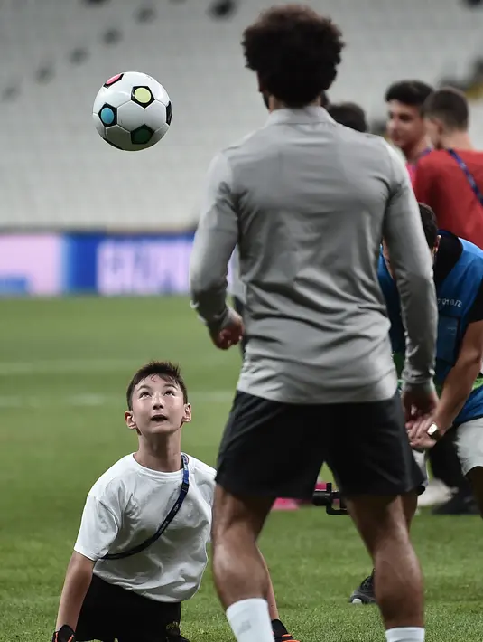 Seorang anak tanpa memiliki kaki menyundul bola saat bermain dengan gelandang Liverpool, Mohamed Salah saat sesi pelatihan jelang bertanding melawan Chelsea pada Piala Super Eropa 2019 di Stadion Taman Besiktas, di Istanbul (13/8/2019). (AFP Photo/Ozan Kose)