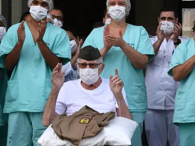 Veteran Perang Dunia II asal Brasil, Ermando Armelino Piveta meninggalkan Rumah Sakit Angkatan Bersenjata setelah pulih dari covid-19 di Brasilia, Selasa (14/4/2020). Kakek 99 tahun itu dipulangkan dari rumah sakit diiringi penghormatan militer dengan terompet dan tepuk tangan. (EVARISTO SA/AFP)