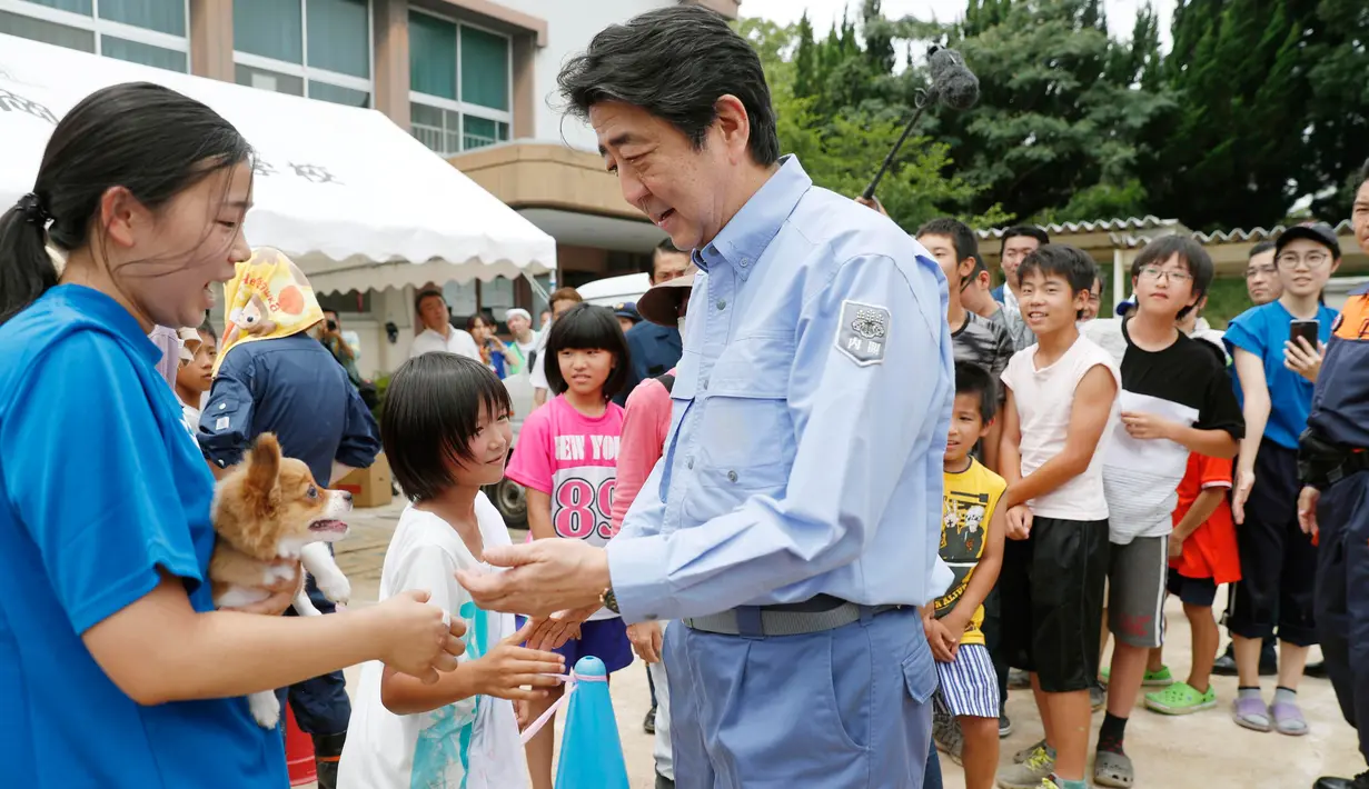 PM Jepang, Shinzo Abe berbincang dengan anak-anak korban banjir di lokasi penampungan di Kurashiki, Prefektur Okayama, Rabu (11/7). Pemerintah menyebut bencana alam ini merupakan yang terburuk dalam tiga dekade terakhir. (Shohei Miyano/Kyodo News via AP)
