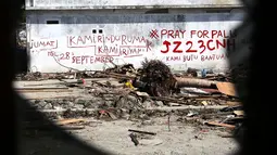 Tulisan cat merah dengan pesan Kami Rindu Rumah Kami dan tagar Pray for Palu menghiasi dinding rumah pasca gempa bumi dan tsunami di Jalan Trans Sulawesi, Palu, Sulawesi Tengah, Kamis (4/10). (Liputan6.com/Fery Pradolo)