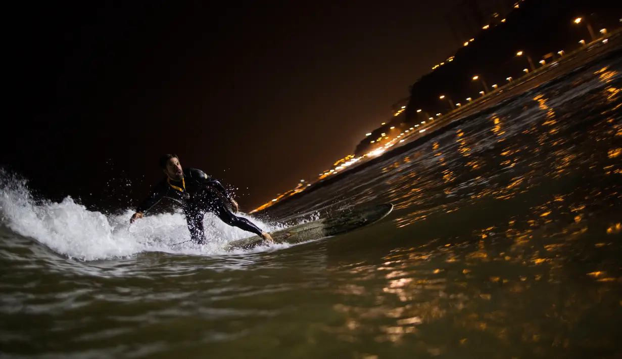 Ernesto Benavides meluncur ke dalam gulungan ombak saat berselancar di pantai La Pampilla, ibu kota Peru, Lima, 26 April 2017. Sekelompok peselancar hardcore memilih bermain selancar pada malam hari. (AP Photo/Rodrigo Abd)