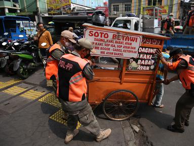 Petugas Satpol PP membawa gerobak pedagang kaki lima (PKL) yang bandel berjualan di trotoar Pasar Tanah Abang, Jakarta, Senin (4/10/2021). Penertiban dilakukan untuk memberikan kenyamanan dan keamanan bagi para pengguna jalan yang melintas di trotoar tersebut. (Liputan6.com/Angga Yuniar)