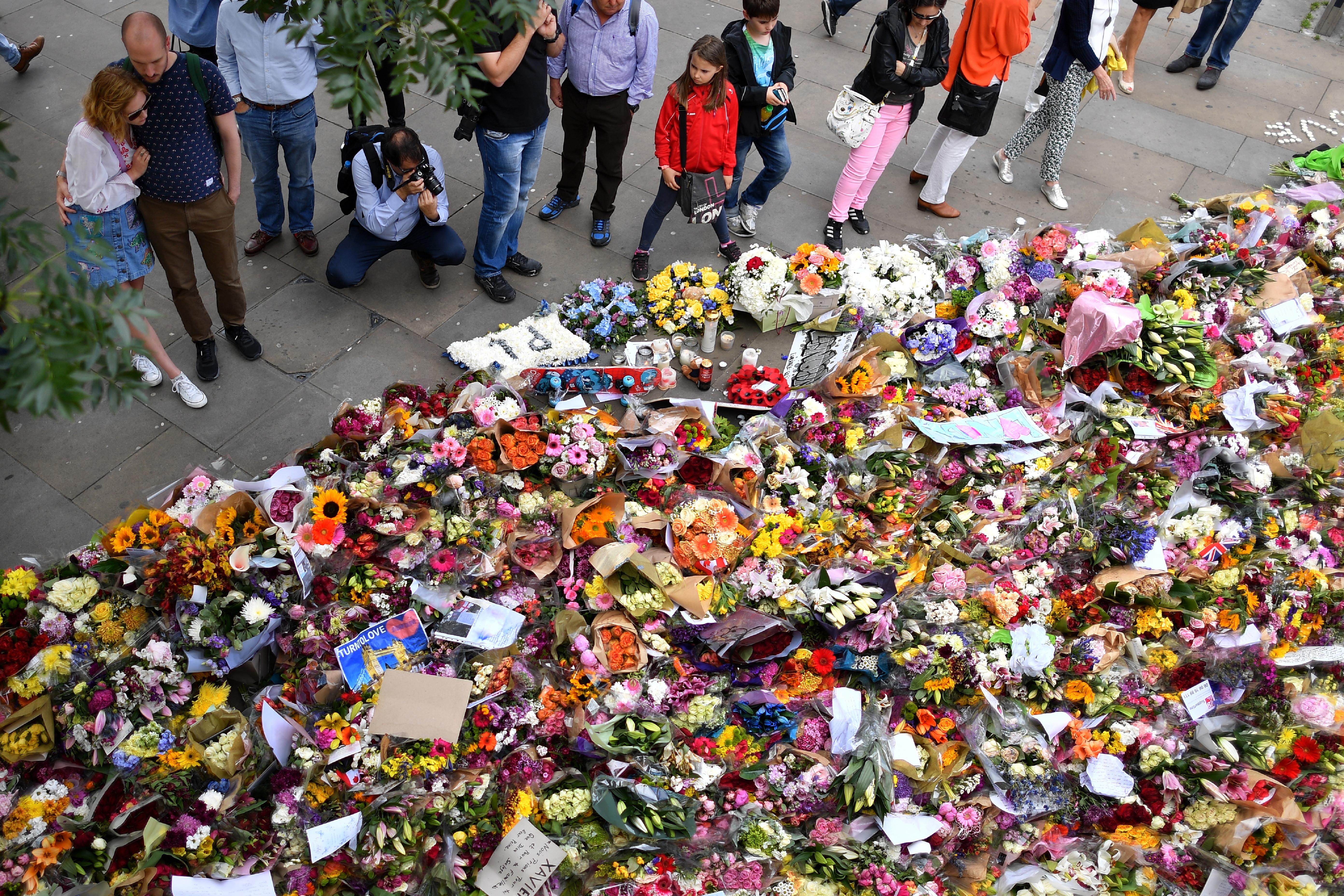 Warga melihat bunga yang tertumpuk di lokasi dekat jembatan London, Inggris (11/6). Pelaku turun dari mobil dengan berjalan kaki ke Borough Market dan menikam orang-orang yang ada di kawasan ramai itu. (AFP PHOTO / Ben STANSALL)
