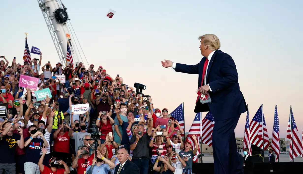 Presiden Donald Trump melemparkan masker dari atas panggung ke kerumunan pendukung saat berkampanye di Bandara Internasional Orlando Sanford di Sanford, Florida, Senin (12/10/2020). Donald Trump kembali berkampanye untuk pertama kalinya usai dinyatakan negatif Covid-19. (AP Photo/Evan Vucci)