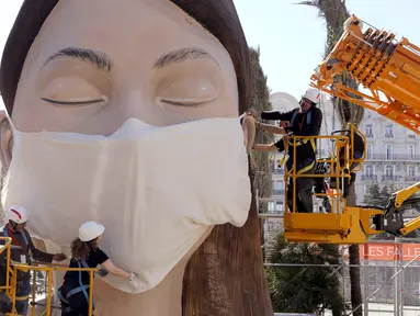 Pekerja memasang masker di salah satu patung raksasa yang akan ditampilkan di festival Las Fallas atau festival api di Valencia, Spanyol, Rabu (11/3/2020). Festival Fallas yang akan berlangsung pada 13 Maret telah dibatalkan karena wabah coronavirus. (AP Photo/Alberto Saiz)