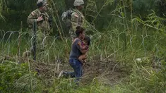 Petugas Garda Nasional Texas berdiri di sepanjang bentangan kawat berduri saat migran perempuan yang membawa seorang anak mencoba menyeberang ke AS, di tepi Rio Grande, seperti yang terlihat dari Matamoros, Meksiko, Kamis (11/5/2023). (AP Photo/Fernando Llano)