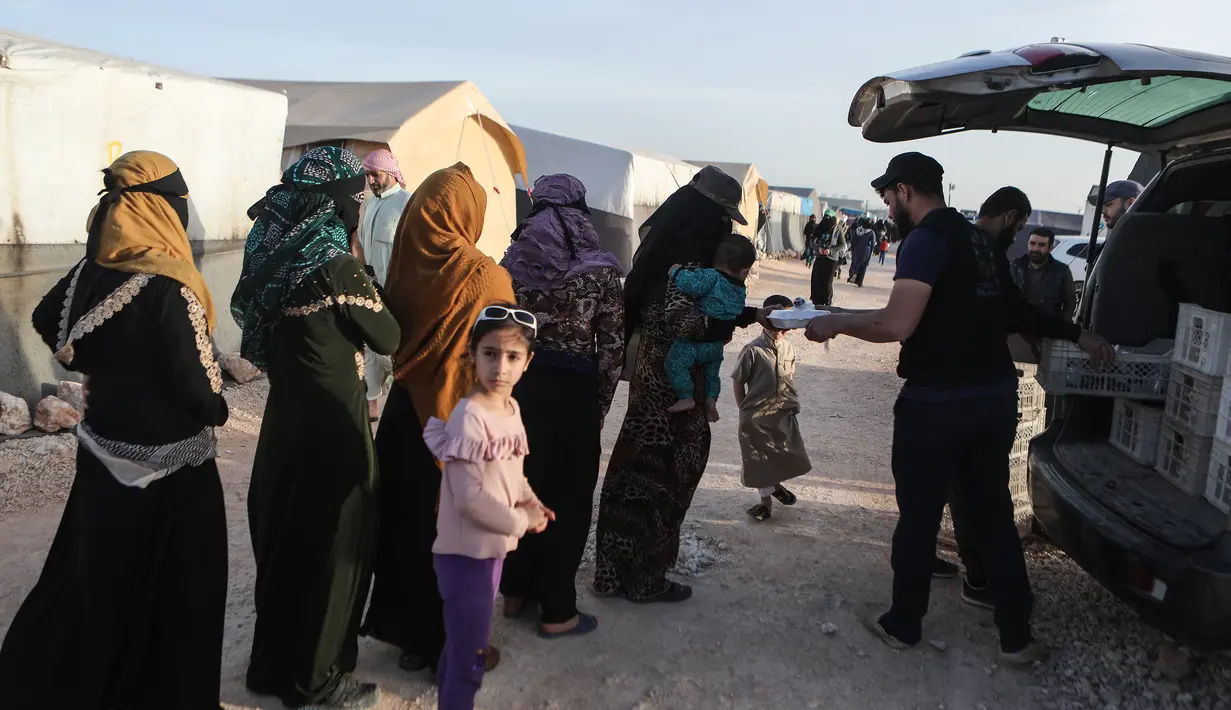 Pengungsi Suriah menerima kotak makanan yang didistribusikan organisasi amal lokal, sebelum berbuka puasa selama bulan suci Ramadhan di kamp pengungsi di pinggiran kota Dana yang dikuasai pemberontak, timur perbatasan Turki-Suriah di provinsi barat laut Idlib (3/4/2022). (AFP/Aaref Watad)