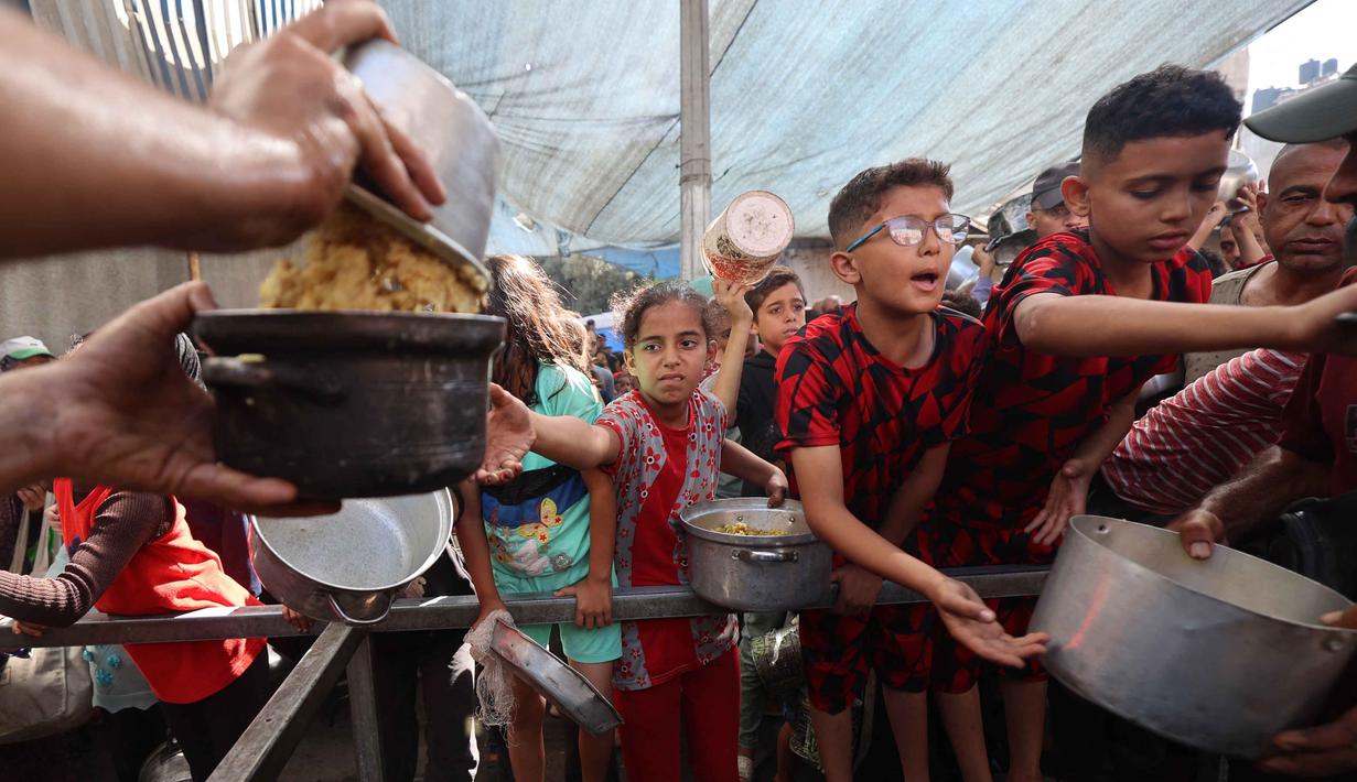 Beberapa anak antre untuk mendapatkan makanan dari dapur amal di kamp pengungsi Nuseirat, yang terletak di bagian tengah Jalur Gaza, pada 21 Oktober 2025. (Eyad BABA/AFP)