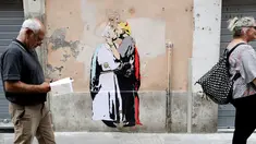 Pejalan kaki melewati mural Presiden AS, Donald Trump dan Paus Francis berciuman di sebuah dinding di Roma, Kamis (11/5). Sebuah keterangan terdapat di sisi lain dari mural yang bertuliskan, "The Good Forgives the Evil." (AP Photo/Alessandra Tarantino)