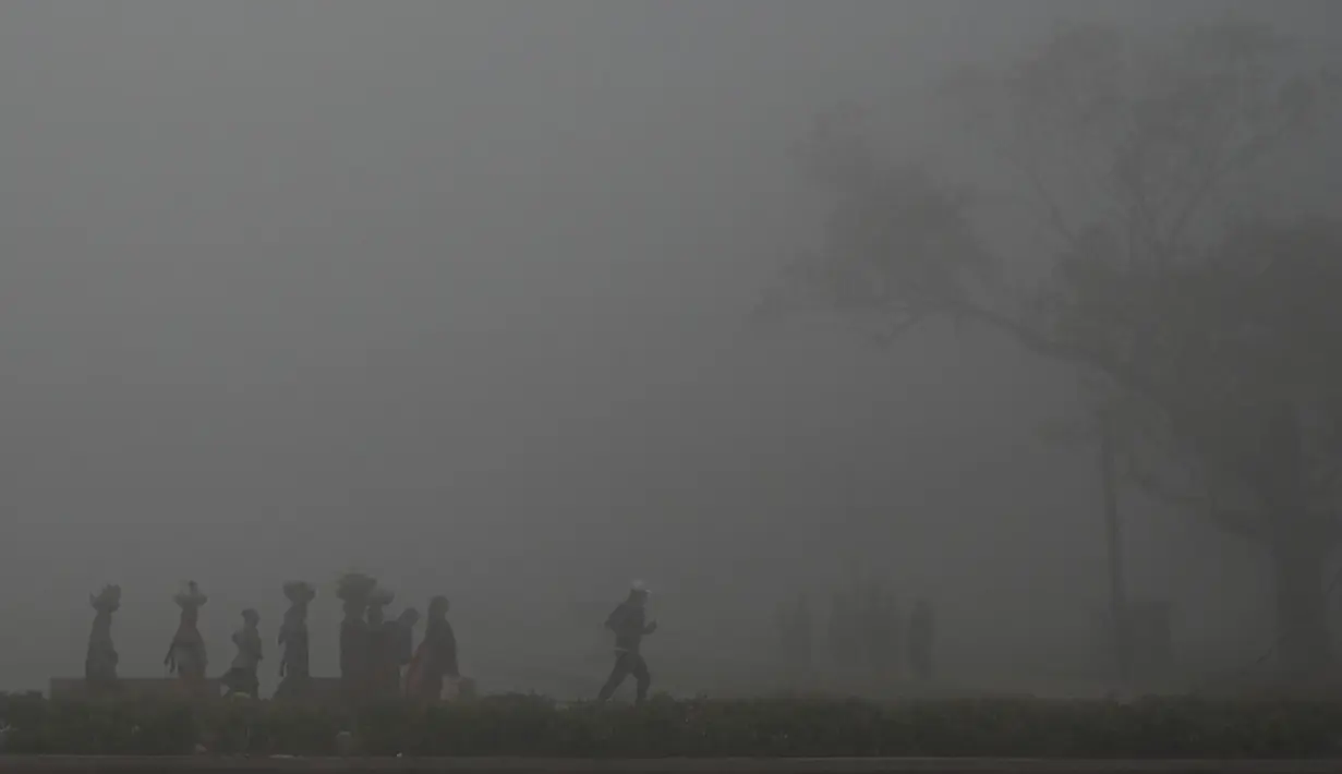 Orang-orang berjalan di sepanjang jalan di dekat gerbang India di tengah kabut asap tebal di New Delhi pada Rabu (22/2/2023). Pada 2020 lalu, platform pengukur tingkat kualitas udara yang bermarkas di Swiss, IQAir mengungkapkan New Delhi merupakan ibu kota paling berpolusi dalam kurun tiga tahun berturut-turut. Tak cuma ibu kota negara, bahkan dari 50 kota paling berpolusi di dunia, 35 di antaranya ada di India. (Arun SANKAR/AFP)