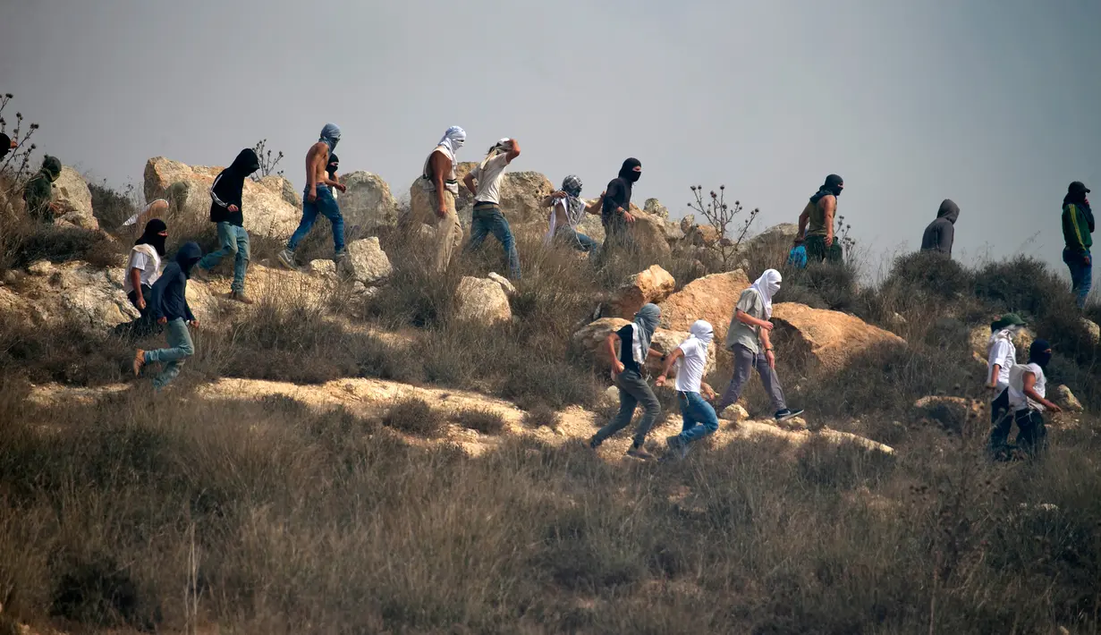Pemukim Israel bertopeng berjalan di tengah-tengah bentrokan dengan pengunjuk rasa Palestina (tak terlihat) selama demonstrasi menentang pembangunan pos terdepan Israel di dekat desa Palestina, Ramallah, Tepi Barat, Kamis (17/10/2019). (JAAFAR ASHTIYEH/AFP)