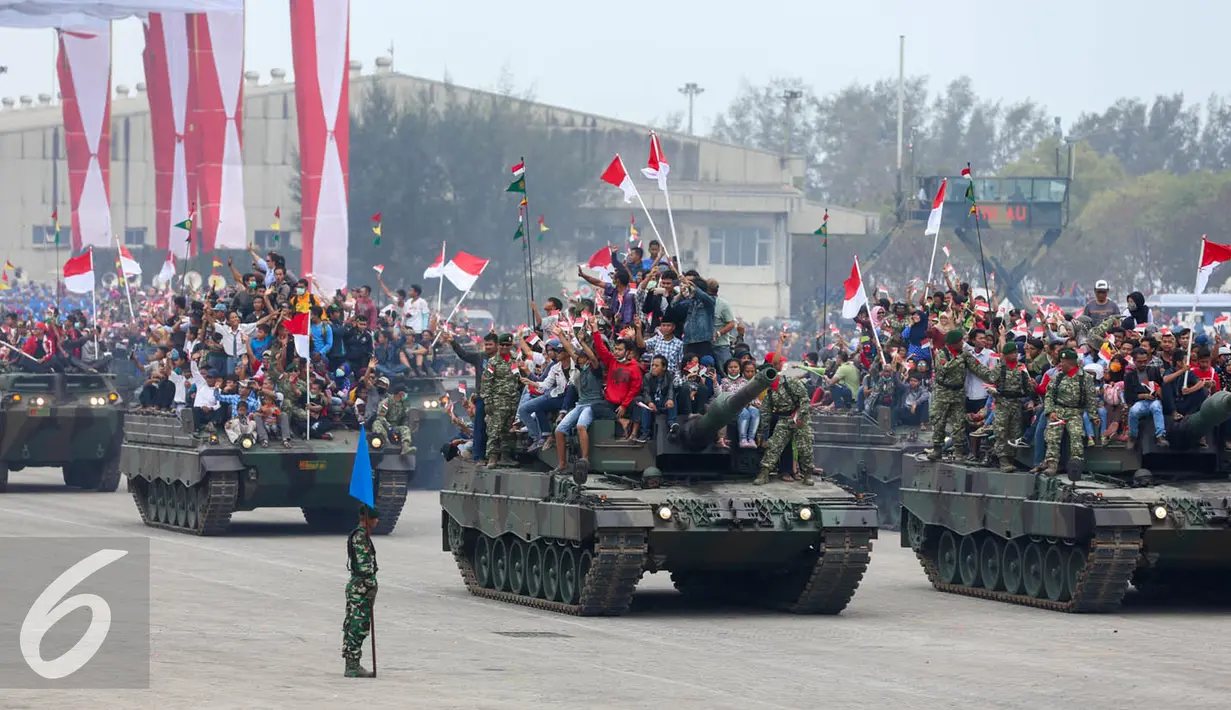 Iringan tank TNI membawa warga yang antusias menyaksikan peringatan HUT TNI ke-70 di Dermaga Indah Kiat, Cilegon, Banten, Senin (5/10/2015). HUT TNI Ke-70 ditandai atraksi tempur tiga matra TNI Angkata Darat, Laut dan Udara. (Liputan6.com/Faisal Fanani)