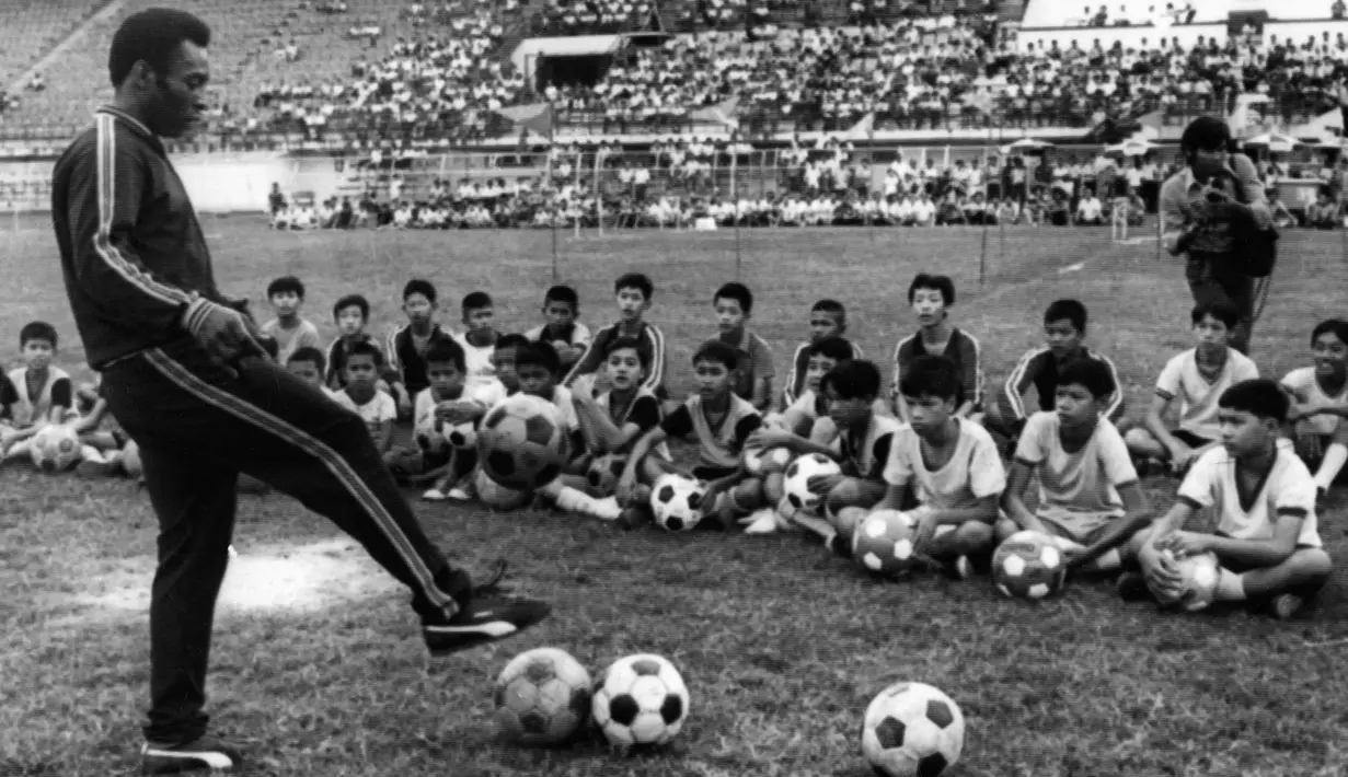 Pemain sepak bola Brasil Edson Arantes do Nascimento atau Pele melatih anak-anak saat perjalanannya ke Bangkok, Thailand, 6 Desember 1974. Kendati sudah memutuskan untuk pensiun, Pele tatap terlibat dalam olahraga dengan bekerja sebagai pandit di televisi dan menjabat sebagai Menteri Olahraga di Brasil antara tahun 1995 dan 1998. (AFP)