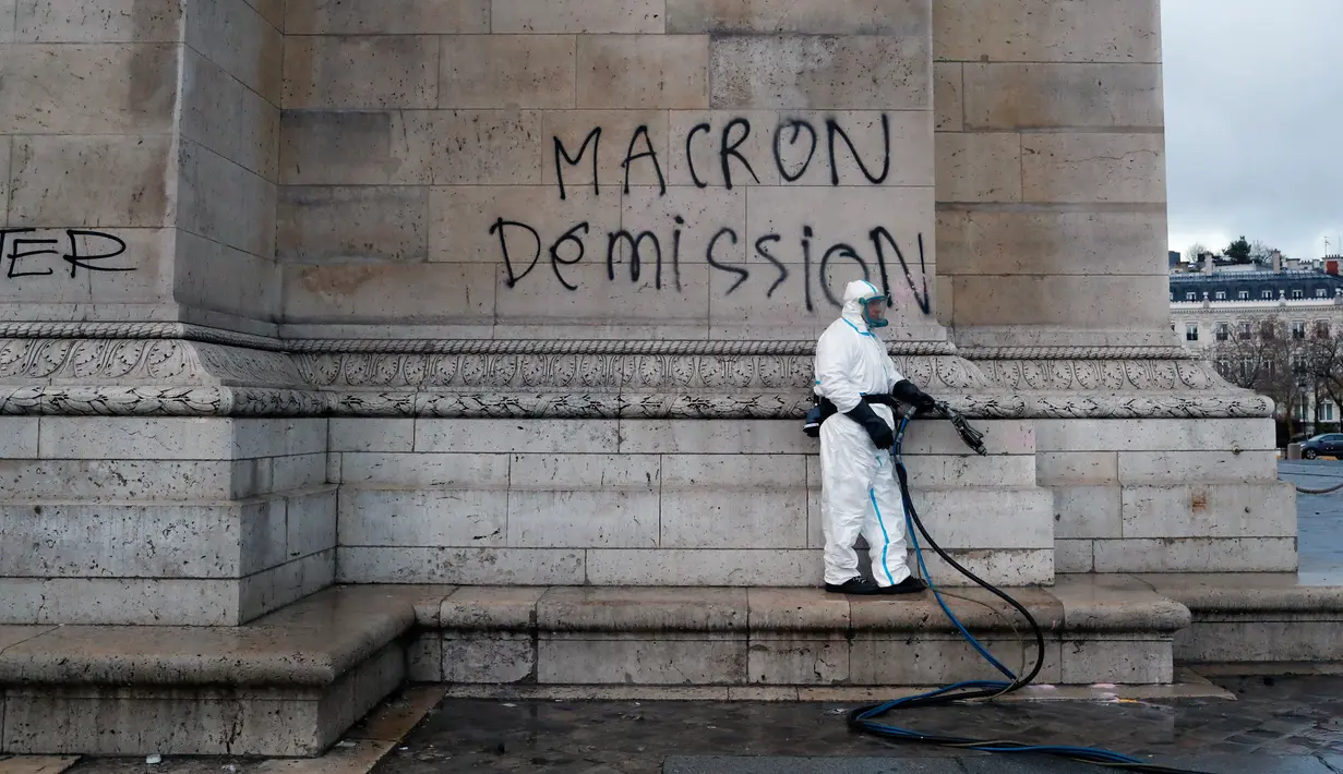 Pekerja membersihkan grafiti bertuliskan 'pengunduran diri Macron' di Arc de Triomphe, Paris, Prancis, Minggu (2/12). Aktivis membakar mobil, menghancurkan jendela, dan menjarah toko saat memprotes kenaikan pajak bahan bakar. (AP Photo/Thibault Camus)