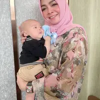 Melihat kebahagiaan Rieta Amalia, ibunda dari Nagita Slavina saat menggendong cucunya Rayyanza, putra kedua dari pasangan Raffi Ahmad dan Nagita Slavina. Di sini, Rieta tampil mengenakan kemeja bermotif bunga bernuansa merah muda yang dipadu dengan hijab polos yang senada. Foto: Instagram.