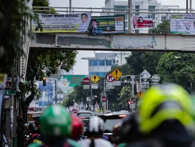 Warga melintasi jembatan penyeberangan orang (JPO) yang terdapat alat peraga kampanye (APK) di Mampang, Jakarta, Rabu (27/2). APK masih menghiasi JPO meski KPU telah melarang pemasangan di sarana dan prasarana publik. (Liputan6.com/Faizal Fanani)