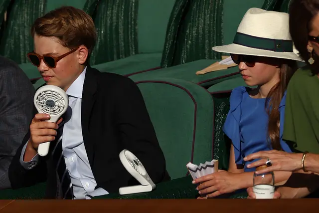 Pangeran George (kiri) dan Putri Charlotte menggunakan kipas untuk mendinginkan diri saat menonton pertandingan final tunggal putra tenis pada hari keempat belas Wimbledon 2026 di The All England Lawn Tennis and Croquet Club di Wimbledon, London barat daya, 12 Juli 2026. (Adrian Dennis/AFP)