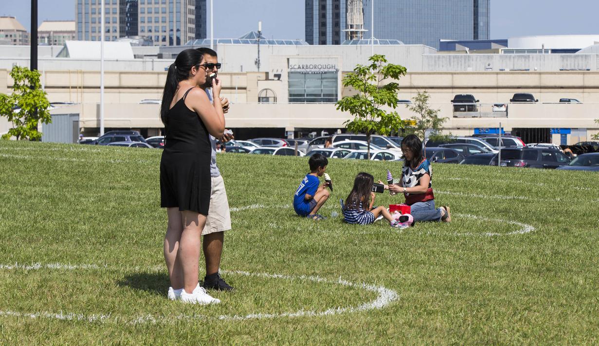 Sejumlah orang tetap berada dalam lingkaran jaga jarak fisik yang dicat di rumput sembari menikmati es krim mereka saat Festival Es Krim Toronto di Toronto, Kanada, Sabtu (15/8/2020). Festival Es Krim Toronto diadakan pada 15-16 Agustus 2020 di tengah pandemi COVID-19. (Xinhua/Zou Zheng)