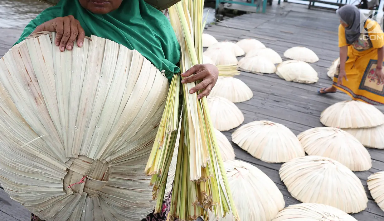 Perajin membawa caping khas Banjar yang selesai dibuat di kawasan Pasar Apung Kuin, Kalimantan Selatan, Senin (26/3). Caping atau tanggui ini biasa digunakan untuk menghindari terik matahari serta hujan. (Liputan6.com/Immanuel Antonius)