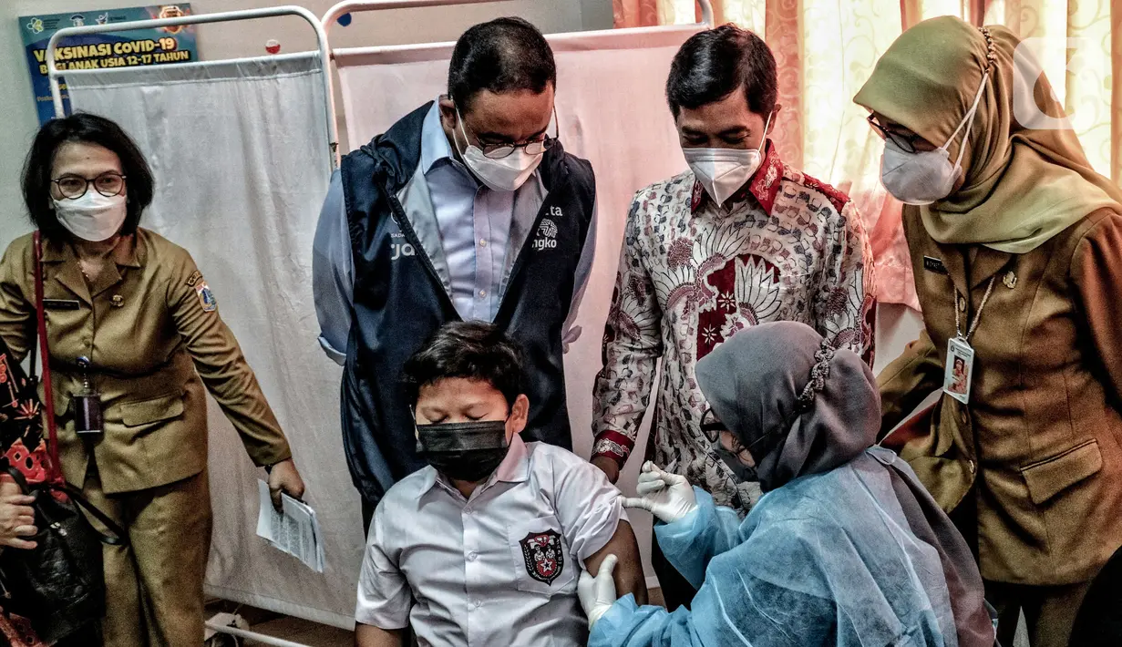 Gunernur DKI Jakarta Anies Baswedan (kedua kiri) melihat seorang murid disuntik vaksin COVID-19 saat meninjau hari pertama pelaksanaan vaksinasi COVID-19 untuk anak 6-11 tahun di SDN Cempaka Putih Timur 03 Pagi, Jakarta, Selasa (14/12/2021). (merdeka.com/Iqbal S. Nugroho)