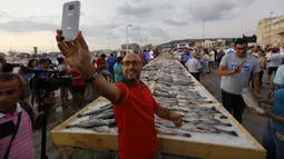 Seorang pria berfoto dengan latar belakang sejumlah ikan yang berhasil memecahkan rekor makanan laut terbanyak di daerah kota pantai Batroun, Minggu (4/9). Menurut panitia, total ikan yang dikumpulnya sebanyak 2 ton 614 kg. (AFP PHOTO/Anwar AMRO)