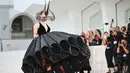 <p>Dalam tampilan dramatis yang mengingatkan kita pada couture Maleficent, Gaga berjalan di karpet merah dengan gaun hitam tebal Christian Dior yang menampilkan garis leher menjuntai dan rok bervolume. (Alberto PIZZOLI / AFP)</p>