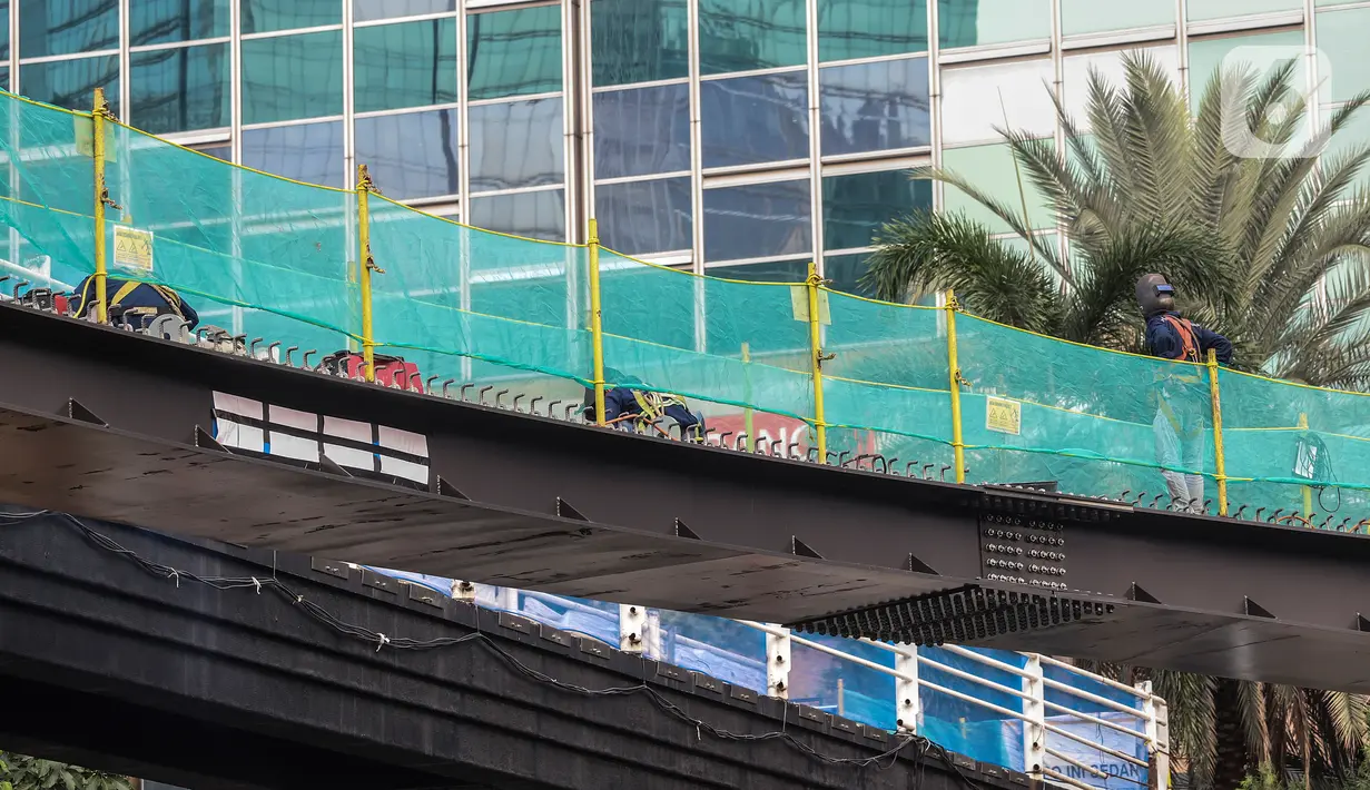 Pekerja menyelesaikan pengerjaan jembatan penyeberangan orang (JPO) dan jembatan penyeberangan sepeda di Karet Sudirman, Jakarta, Jumat (8/10/2021). Jembatan penyeberangan dengan konsep modern yang dilengkapi anjungan bertema kapal pinisi ini sudah mencapai 70 persen. (Liputan6.com/Johan Tallo)