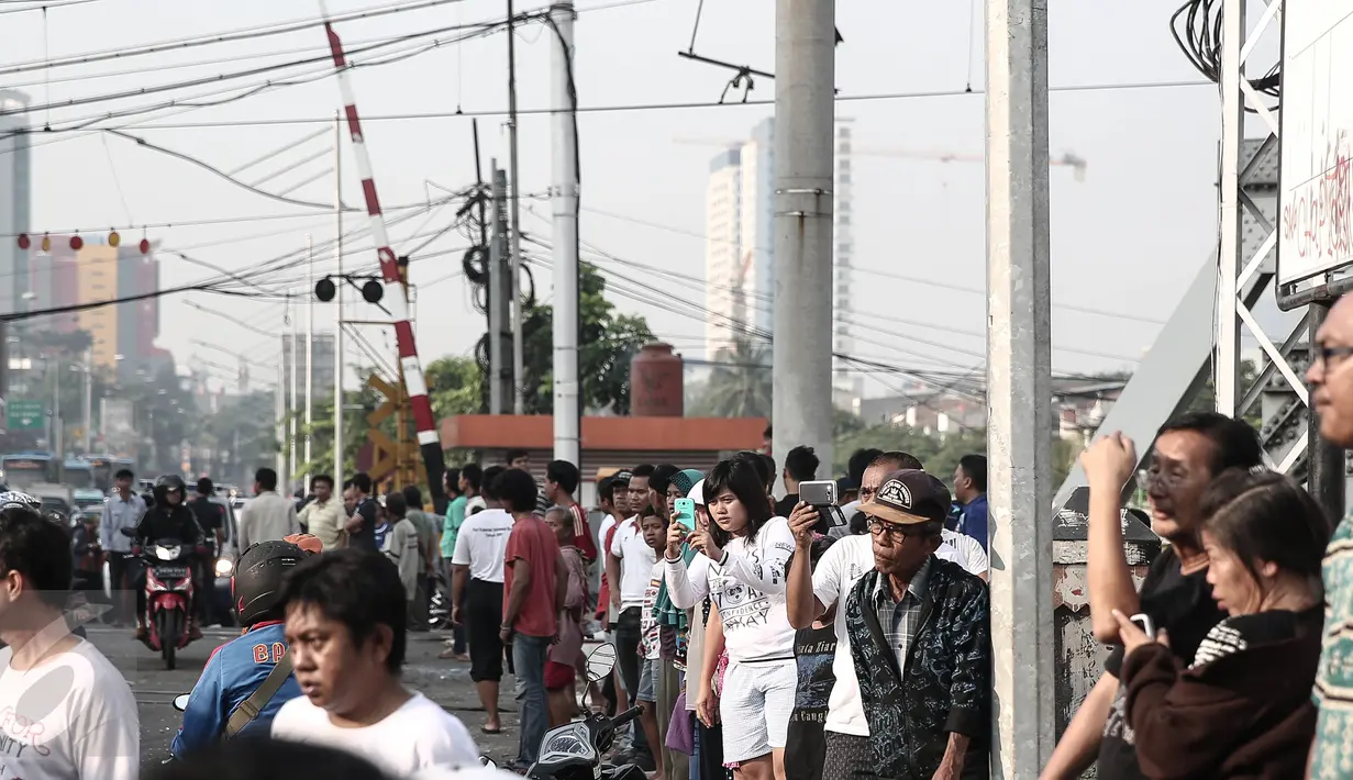 Sejumlah warga berkumpul di lokasi kecelakaan bus TransJakarta yang ditabrak kereta api Senja Utama Solo di perlintasan kereta Mangga Dua, Jakarta, Kamis (19/5). Saat insiden, bus TransJakarta sedang tidak mengangkut penumpang (Liputan6.com/Faizal Fanani)