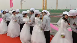 Pengantin pria dipersilahkan mencium pengantin wanita mereka usai upacara pernikahan, Beijing, Senin (12/12). Kelima pekerja ini kompak untuk menggelar upacara pernikahan di tempat proyek mereka bekerja yaitu sebuah bandara. (AFP PHOTO)