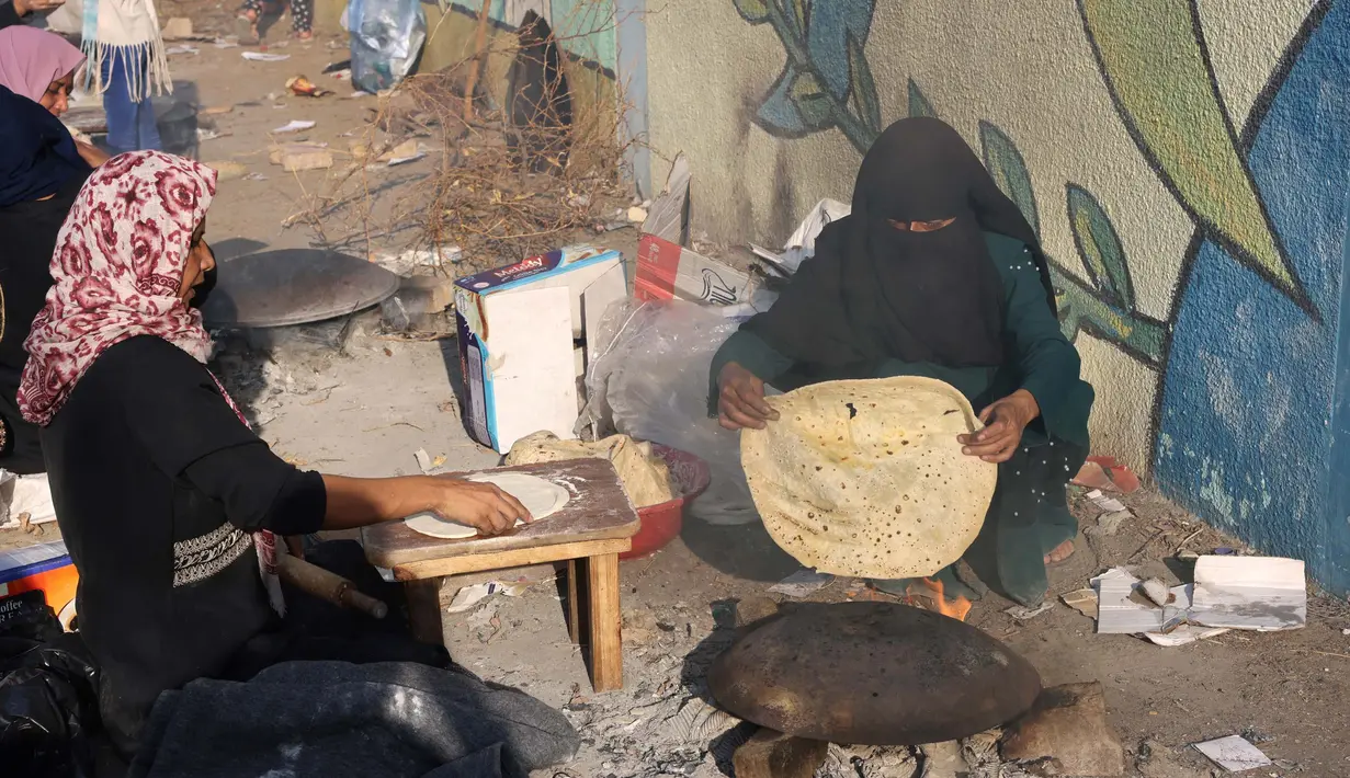 Para wanita Palestina membuat roti tidak beragi tradisional di atas api terbuka di salah satu lokasi penampungan pengungsi pada 27 Oktober 2023. (SAID KHATIB/AFP)