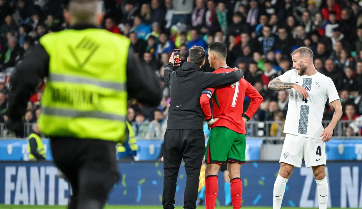 Fans nekat menerobos lapangan dan berswafoto dengan bintang Portugal, Cristiano Ronaldo, saat melawan Slovenia pada laga persahabatan di Stadion Stozice, Ljubljana, Rabu (27/3/2024). Portugal menyerah dua gol tanpa balas dari tuan rumah. (AFP/Jure Makovec)
