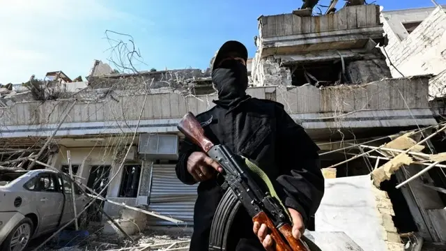 Seorang anggota pasukan keamanan pemerintahan baru Suriah berjaga di lokasi serangan Israel di wilayah Damaskus, tempat para pemimpin Palestina diketahui tinggal. (Louai Beshara/ AFP)