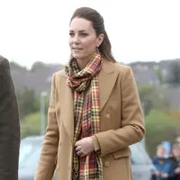 Ini saat Kate Middleton berkunjung ke Skontlandia, mengenakan long coat dari Massimo Dutti berwarna camel netral yang klasik dengan syal kotak-kotak Strathearn yang agak pop, dan celana high-waisted bernuansa senada. Foto: Bustle.