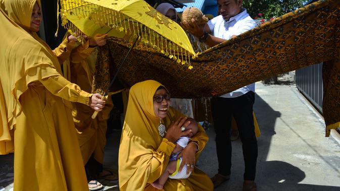 Tokoh adat dan agama mengendong bayi saat orang tua (ayah bayi) membelah kelapa pada ritual 'peutron tanoh aneuk' (turun tanah anak) di Banda Aceh, Aceh, Senin (15/7/2019). Ritual turun tanah anak dilaksanakan pada saat bayi berusia 44 hari. (CHAIDEER MAHYUDDIN / AFP)